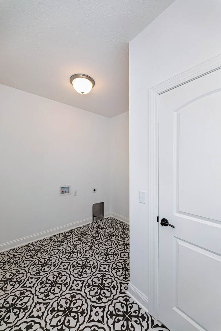 White door with black handle, black and white patterned tile floor, white plaster walls, ceiling light fixture