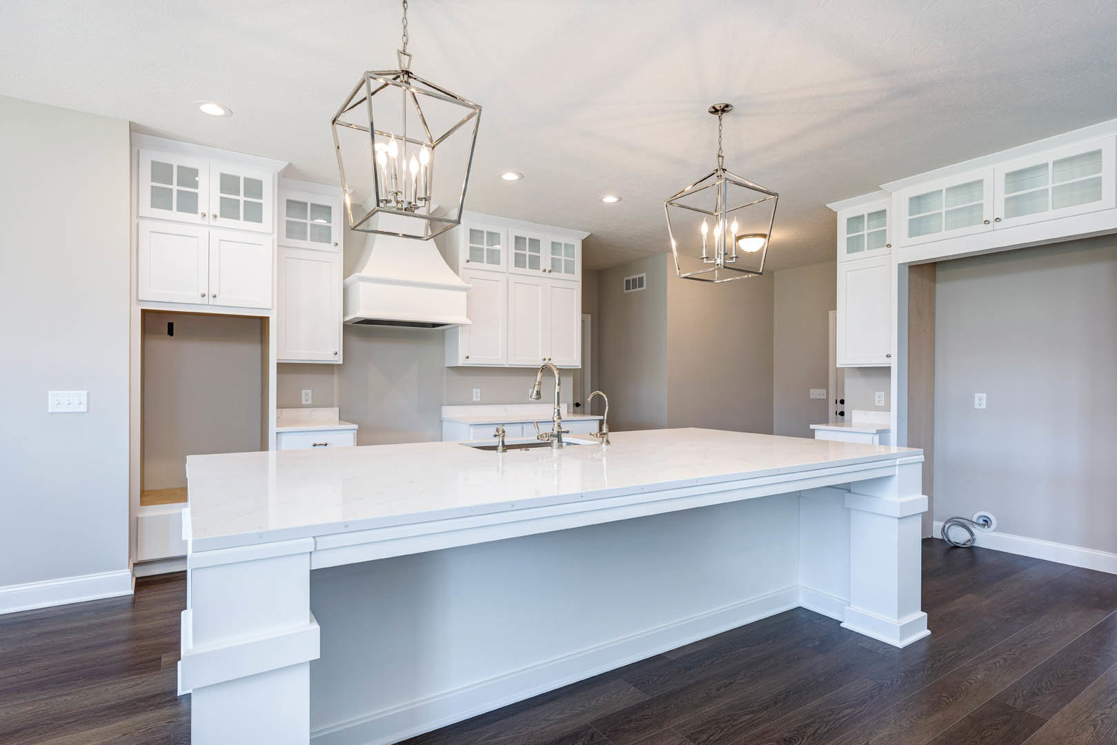 Spacious kitchen featuring a large white island countertop with silver faucets, modern tile flooring, white cabinetry, ceiling-mounted light fixture, and a close-up of a