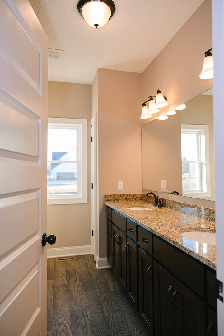 Bathroom featuring marble countertop, large wall mirror, dark wood flooring with vent, white-framed window, modern faucet, and contemporary light fixture