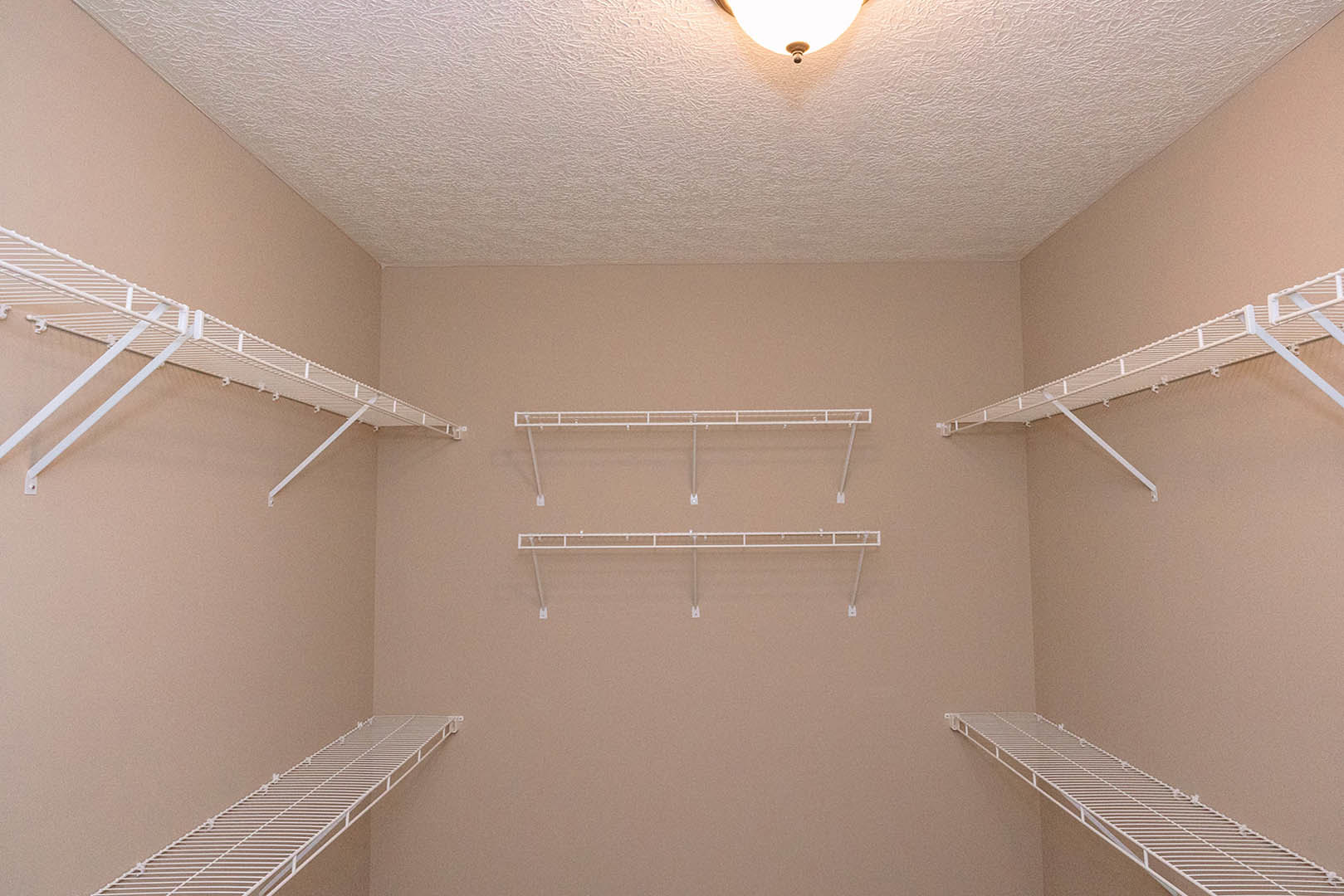 Walk-in closet with white metal shelving, hanging bar, plaster walls, and recessed ceiling light fixture