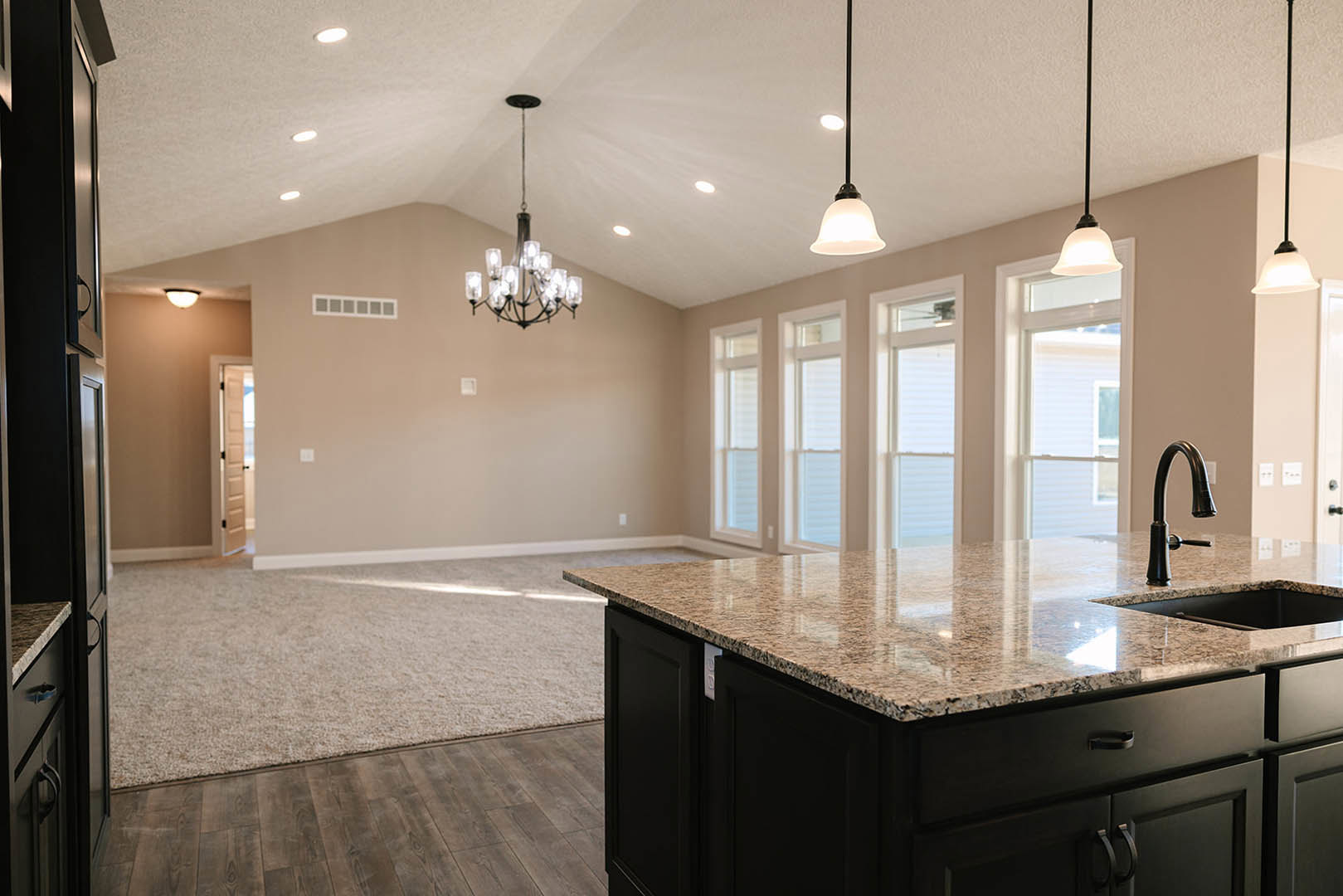 Granite kitchen island with black faucet, white tile backsplash, wood cabinetry, and glass chandelier overhead