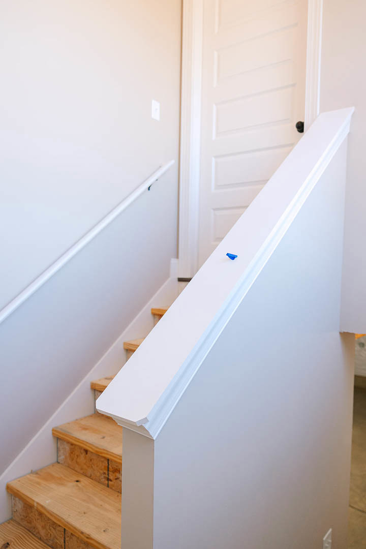 White-painted wooden staircase with hardwood steps, white plaster walls, and a blue pin placed on the top step
