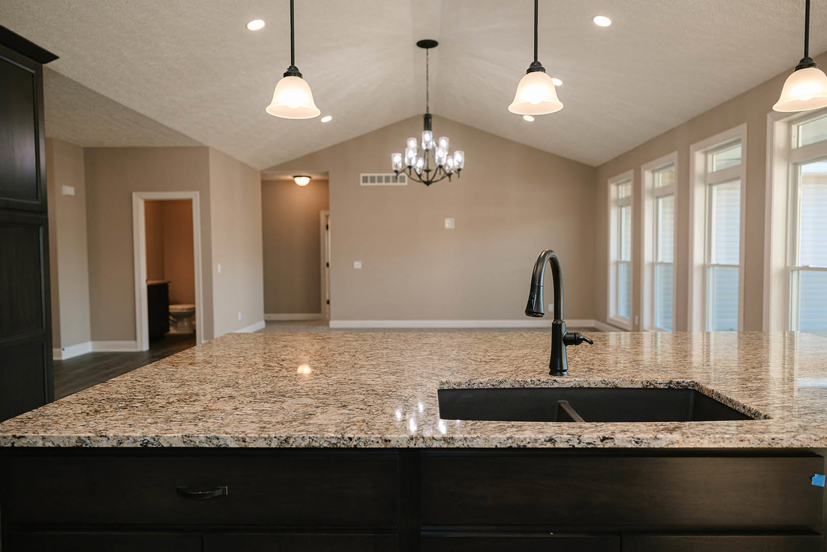 Modern kitchen featuring a black countertop, stainless steel sink with chrome faucet, tile backsplash, white cabinetry, and a crystal chandelier hanging from the ceiling