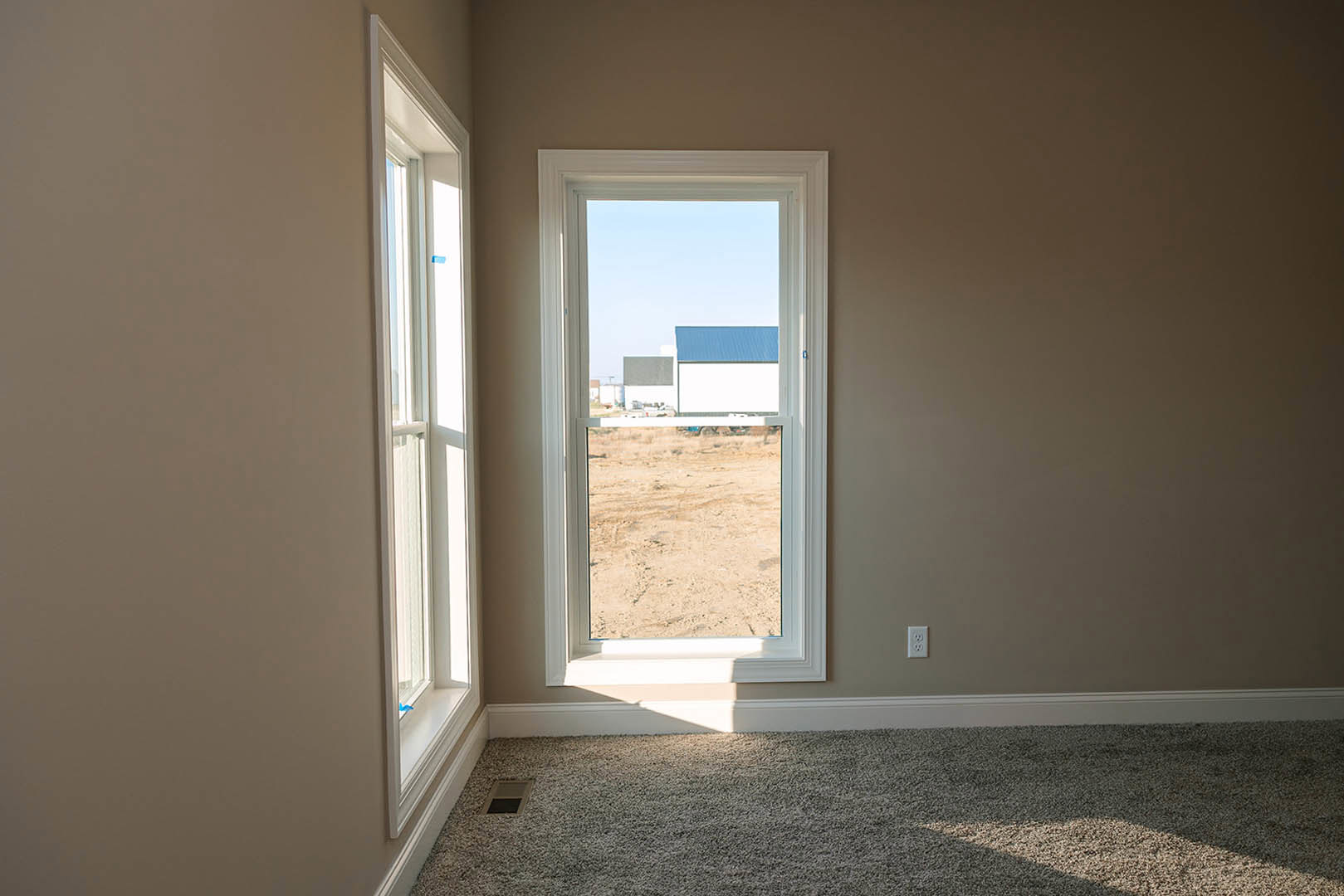 Carpeted floor with white-framed window overlooking a field and distant buildings, wall painted light neutral, ceiling vent visible