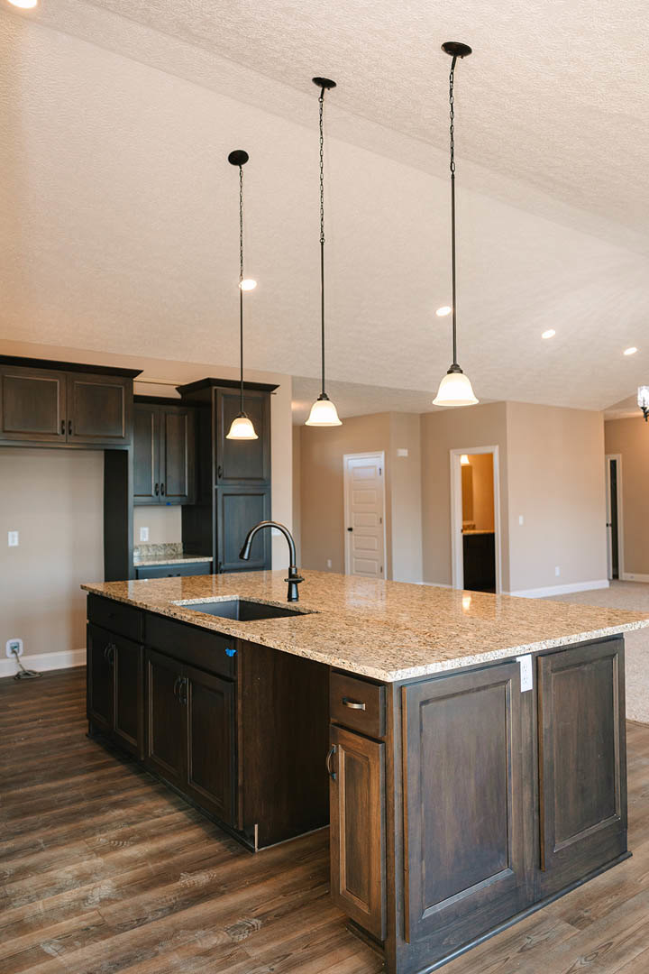 Spacious kitchen featuring a large central island with built-in sink, white cabinetry with black hardware, light tile backsplash, and wood flooring