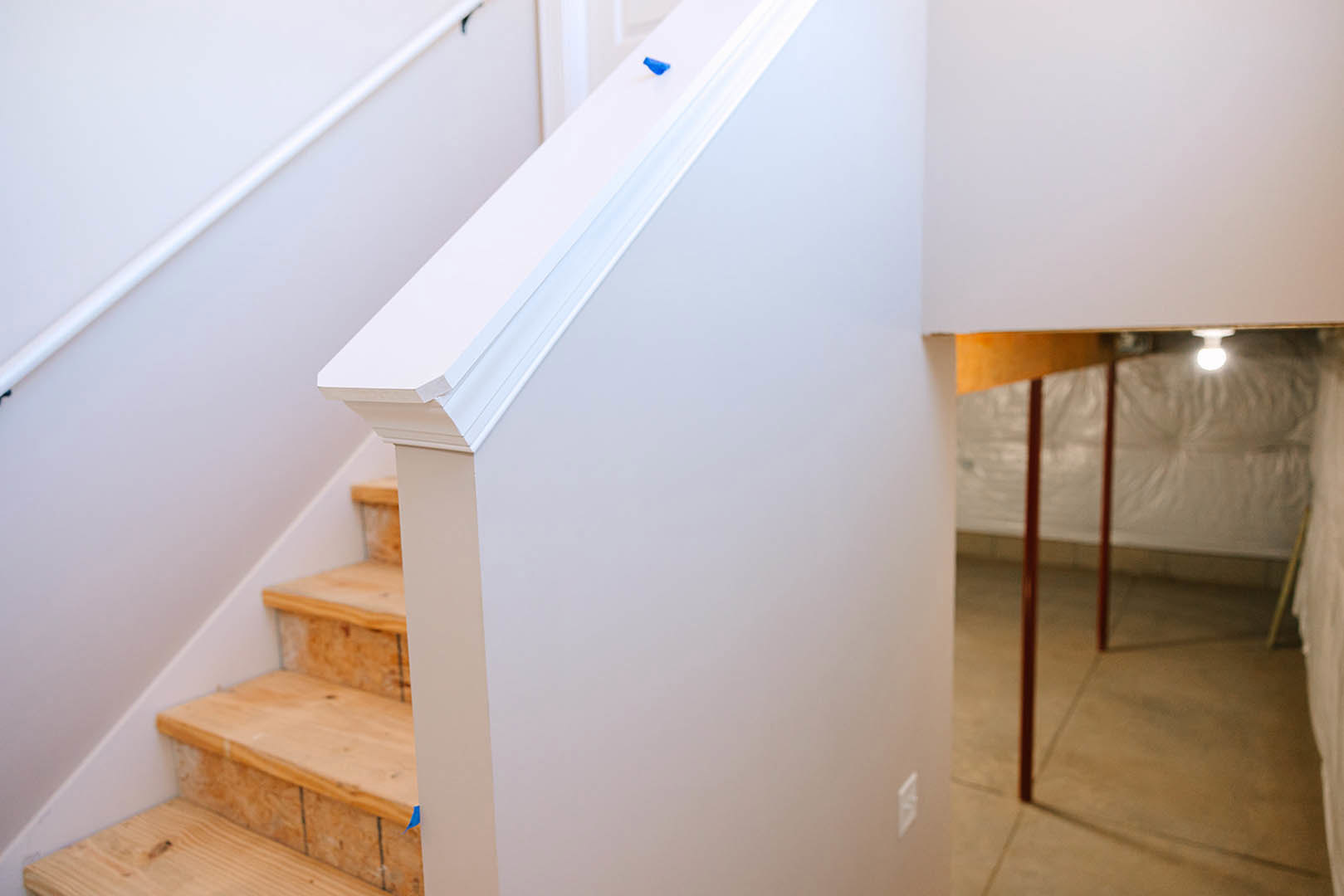 White staircase with natural wooden steps beside a smooth white wall, red metal pole accent, and ceiling light fixture.
