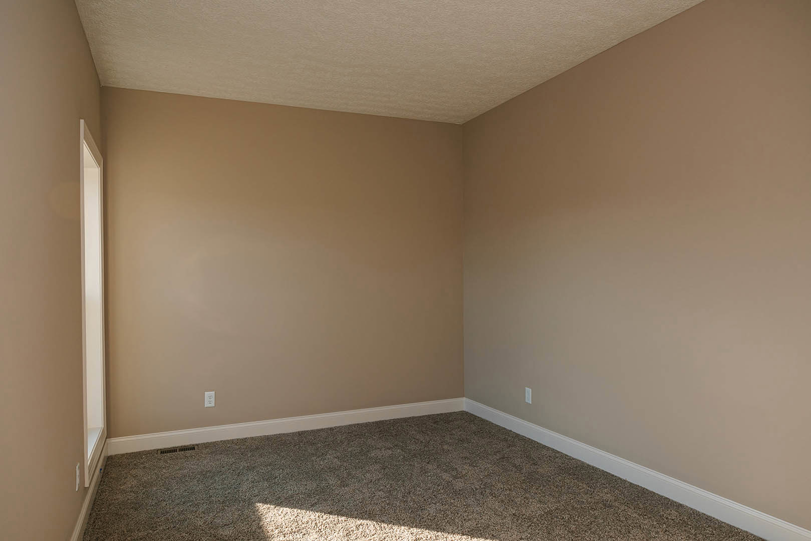Beige-walled room with plush tan carpet, white door, ceiling light, and simple baseboard molding