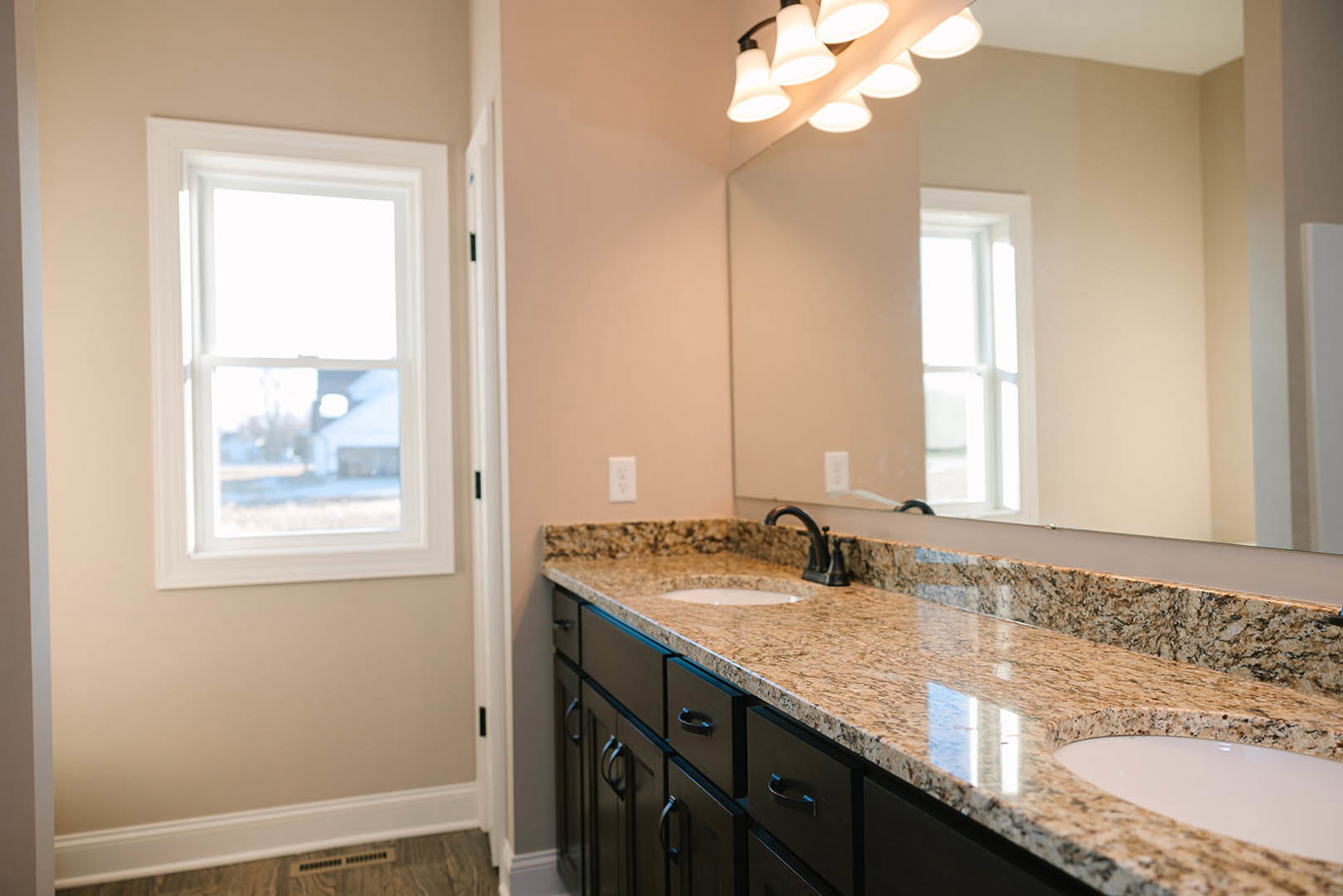 Marble bathroom countertop with dual white sinks, large framed mirror, modern light fixture, and window overlooking snowy landscape