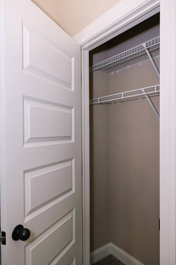 White closet interior with built-in metal shelves, white plaster walls, and a close-up view of the door and handle.