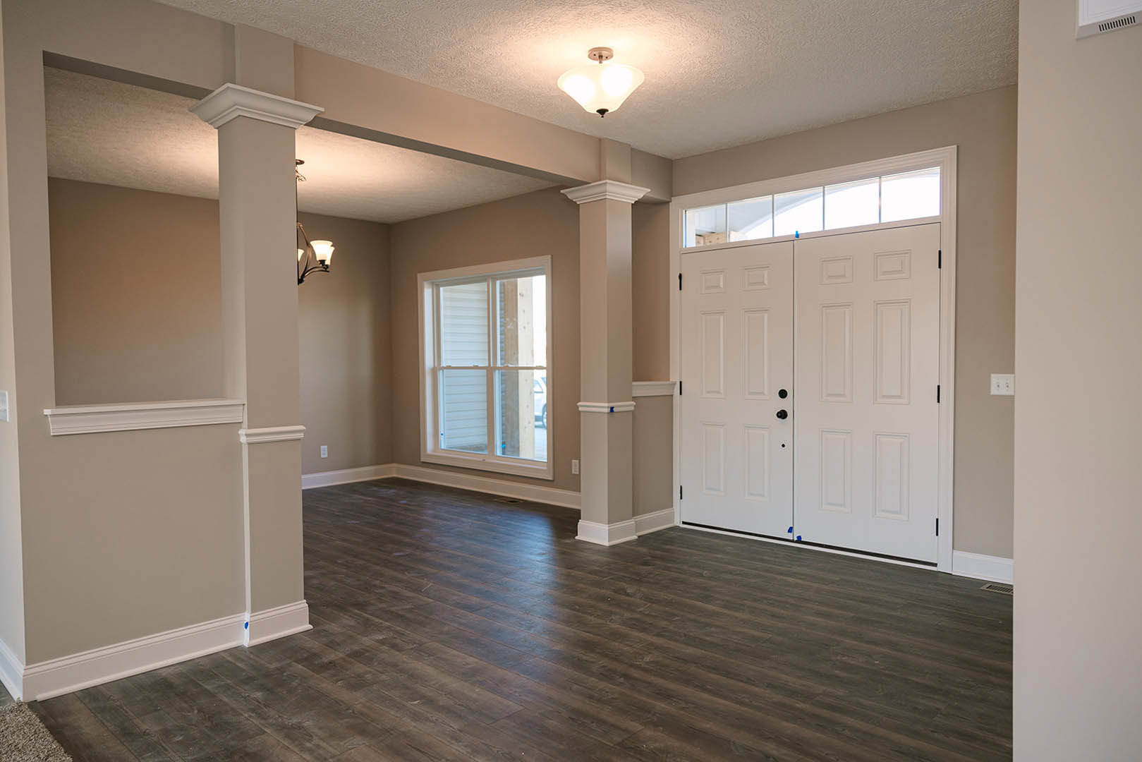 White double doors with transom window, wood flooring, white walls, ceiling light fixture, window with blue decor item