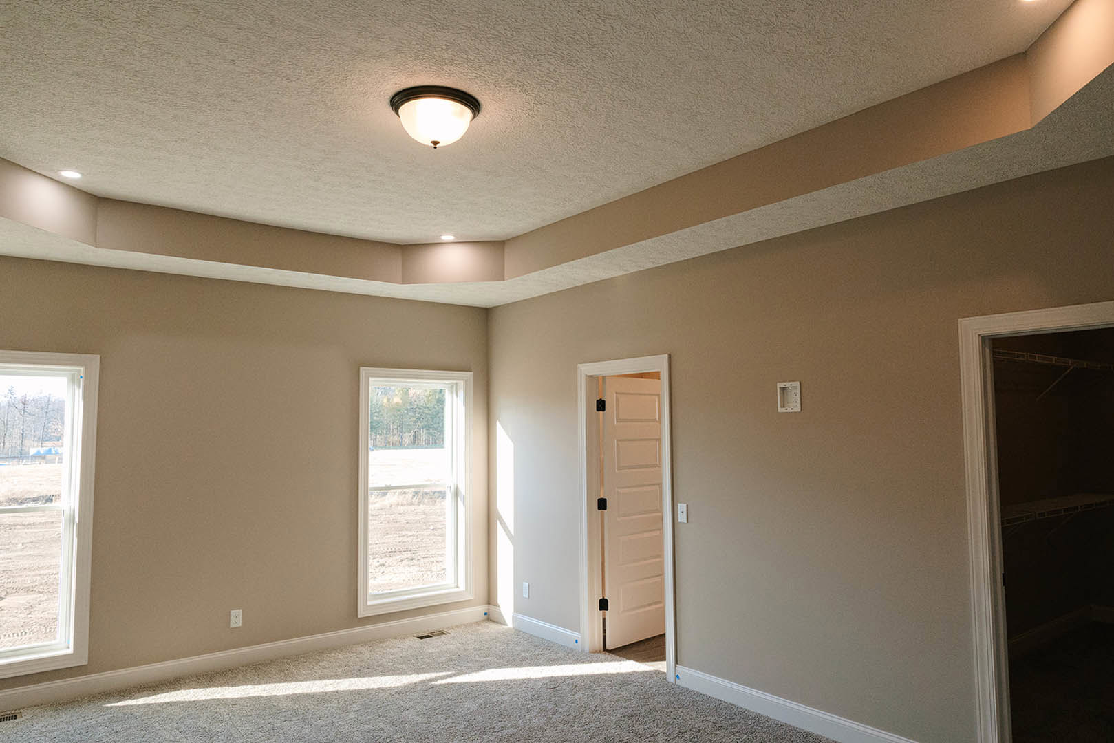 White plaster walls and ceiling with recessed light fixture, single window overlooking grassy field, paneled door with black handle, built-in shelf in dark door frame, simple