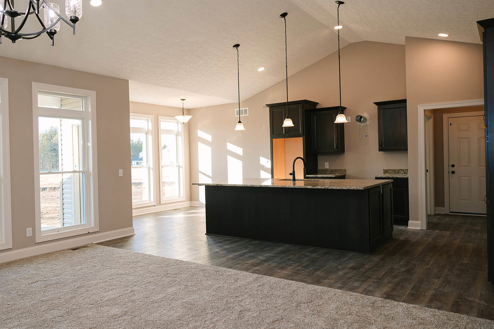 Open-concept kitchen and living room featuring a large black countertop island with integrated black sink, white cabinetry with black hardware, modern chandelier, and window