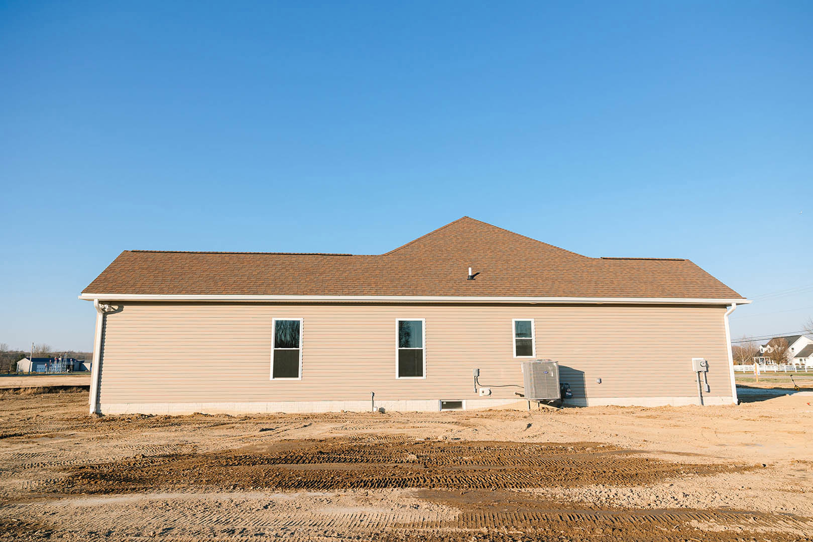 Partially built house with white-framed window, exposed siding, dirt foreground, and clear blue sky