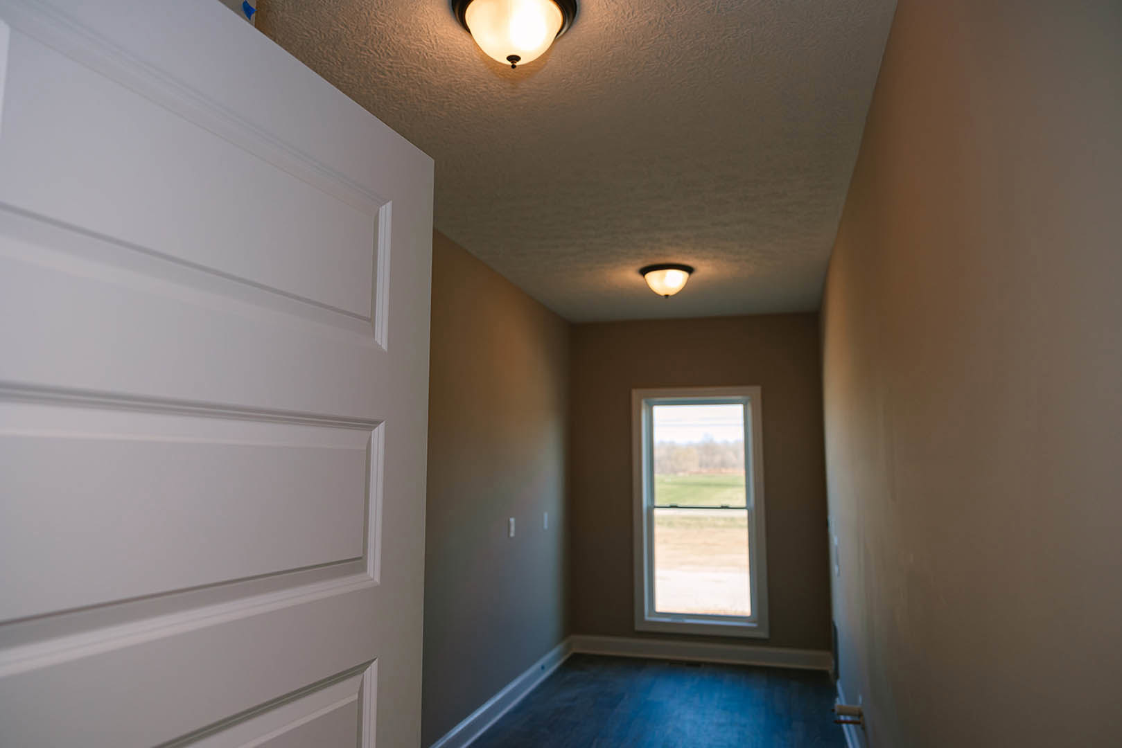Hallway with white paneled door, blue tile floor, window overlooking a field, and modern ceiling light fixture
