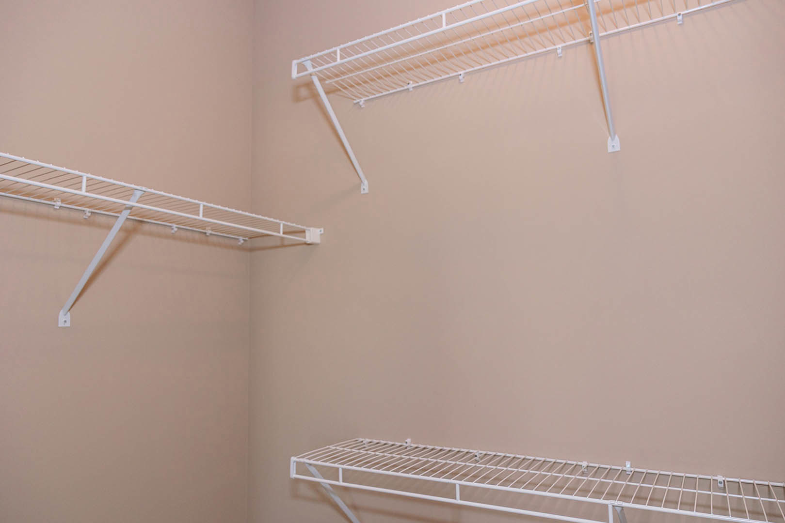 White wire shelving unit with metal rods mounted on a wall above a brown surface in a residential room.