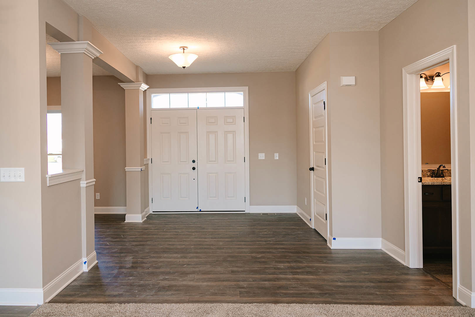 Hallway with white paneled doors, black knobs, wood laminate flooring, white plaster walls, ceiling molding, and a modern light fixture
