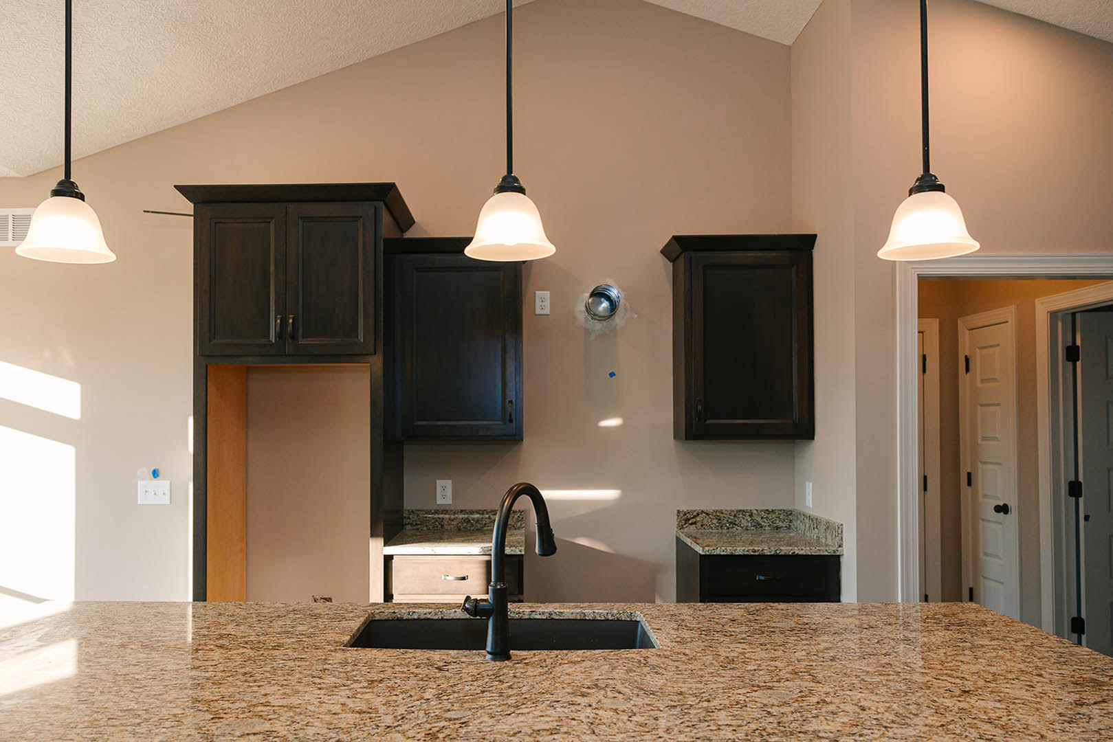 Modern kitchen featuring dark cabinetry, stainless steel sink, stone countertop, built-in appliances, and pendant lighting above the workspace.