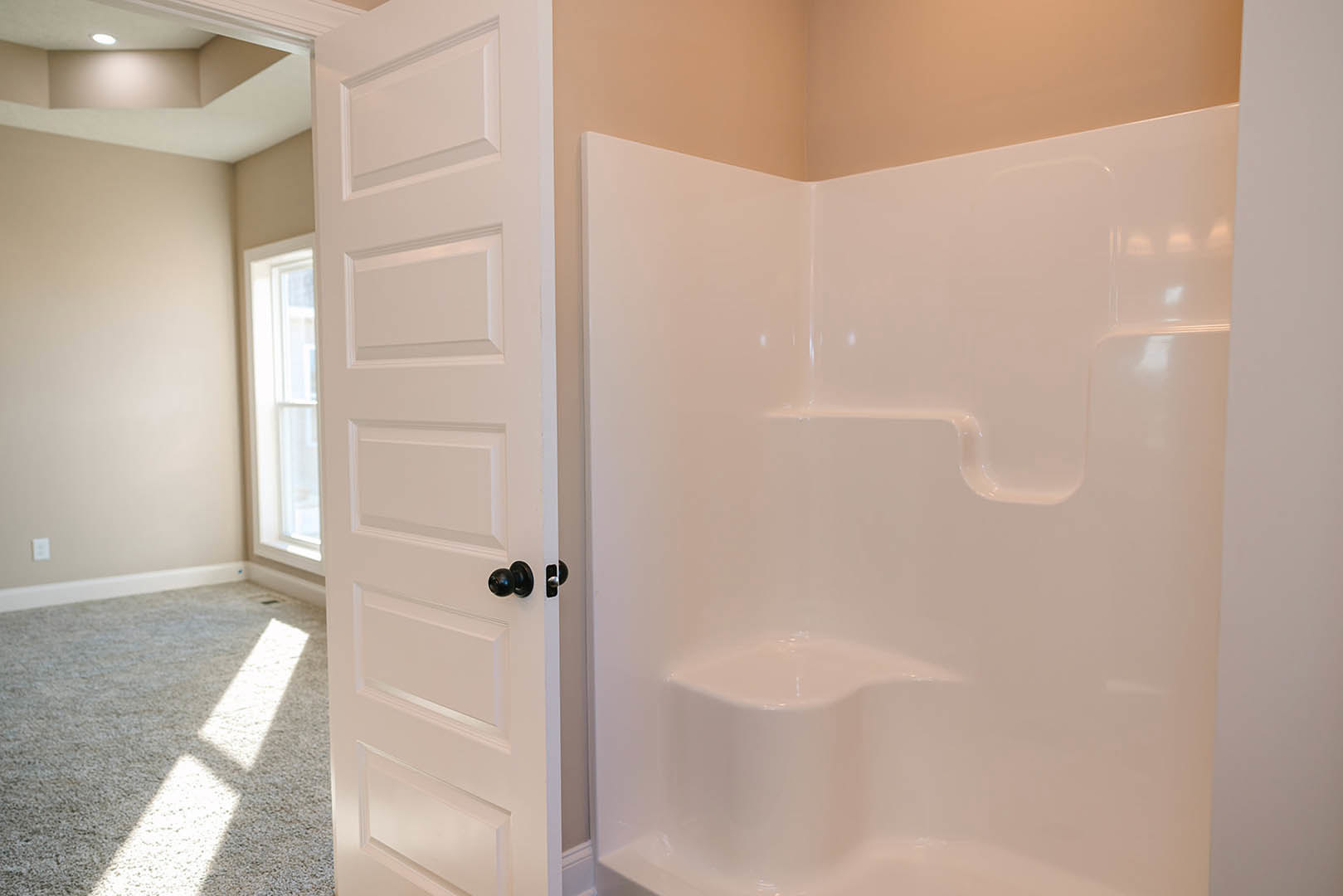 White tile shower stall with glass door, black hardware, and adjacent white bathroom walls