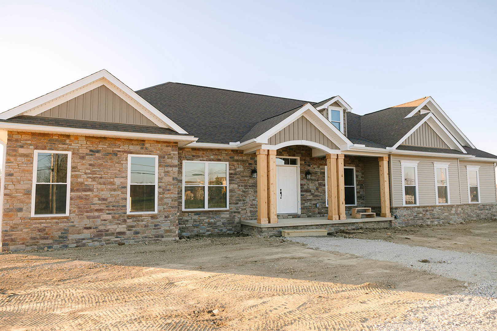 Stone and siding exterior home with white framed windows reflecting trees, white front door, and paved driveway