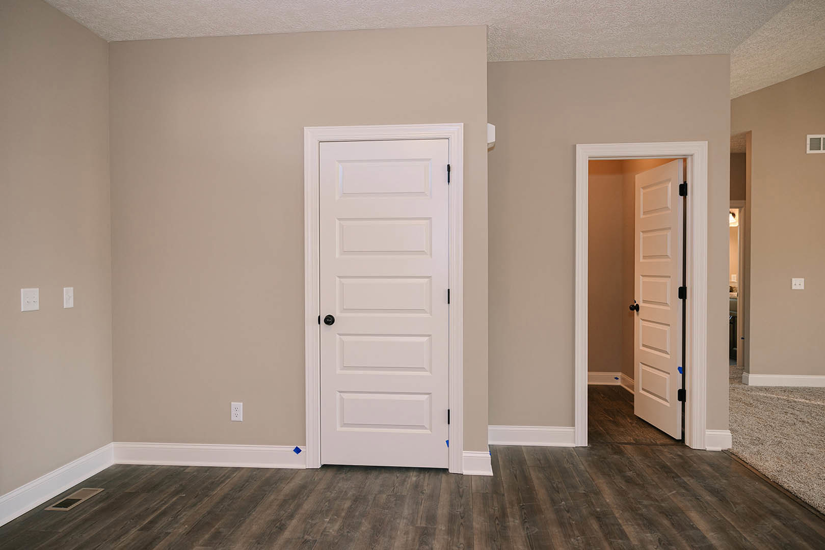 White paneled doors with black hardware, light wood flooring, white baseboards, and a floor vent in a bright interior room