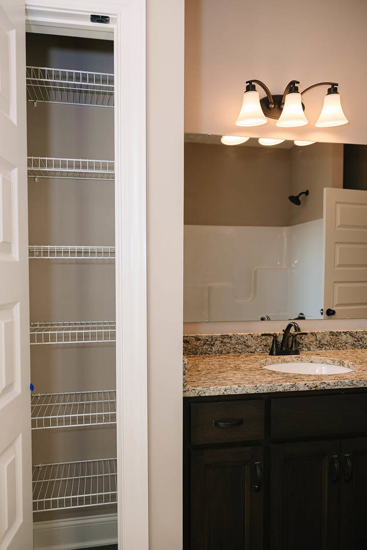 Modern bathroom featuring a rectangular sink with chrome faucet, large frameless mirror, light gray tile backsplash, and white cabinetry with stone countertop