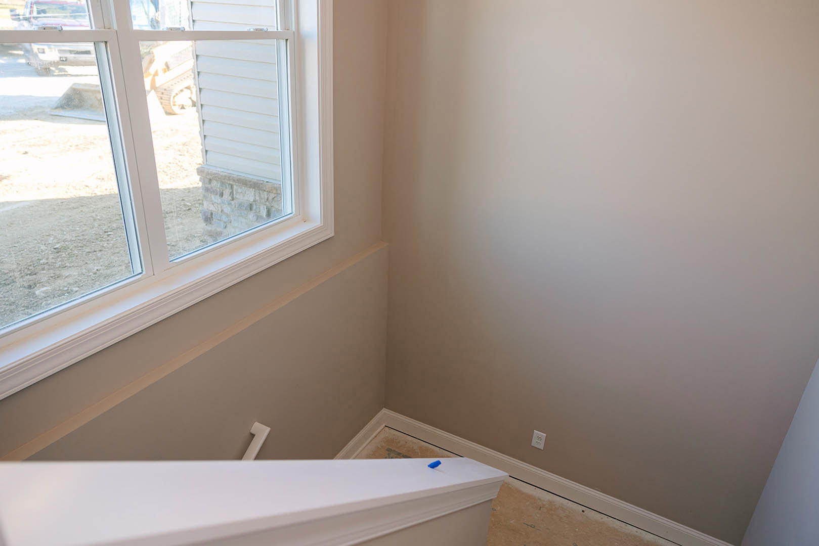 White staircase with wood treads beside large window, sunlight illuminating neutral plaster walls and light hardwood floor