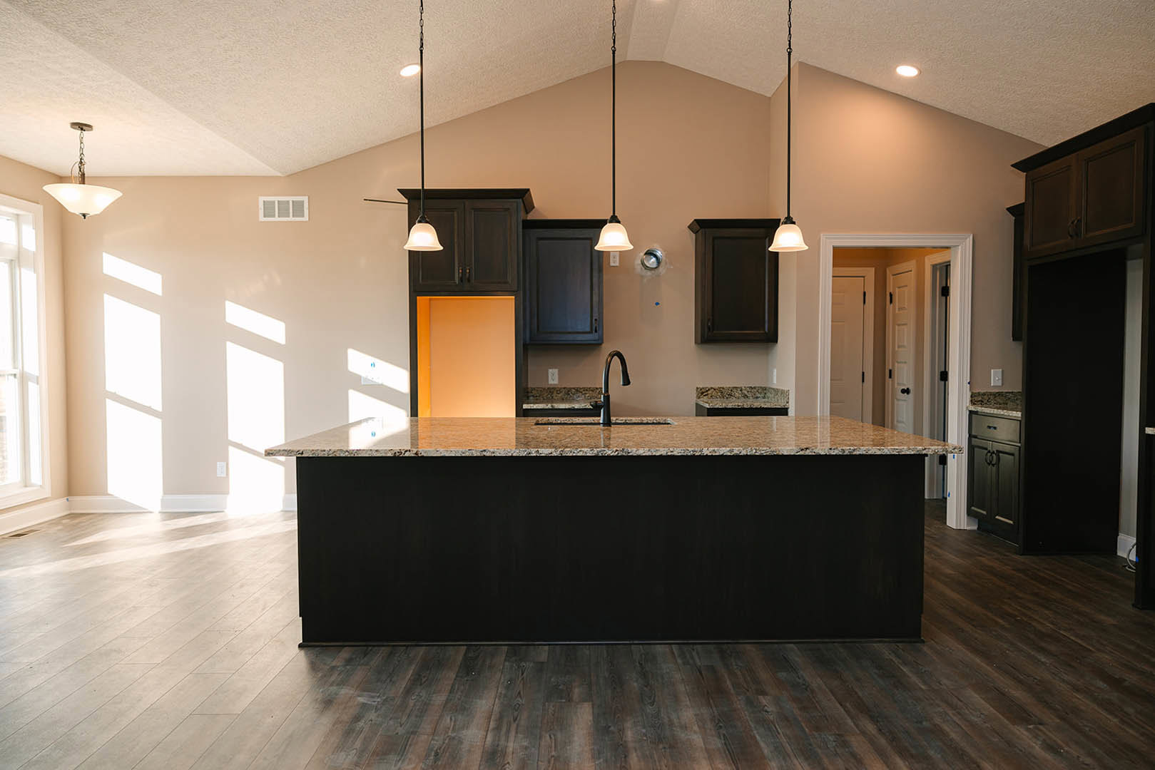 Black kitchen island with matching countertop and integrated sink, surrounded by light cabinetry, pendant bell-shaped light fixture overhead, and close-up view of a dark door.