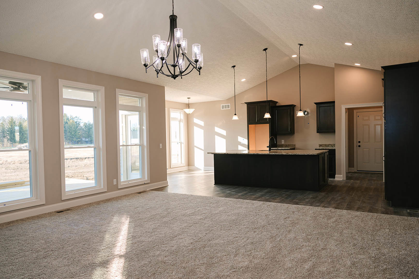 Spacious open floor plan featuring a modern kitchen with black marbled countertops, black refrigerator, white cabinetry, and a prominent chandelier; white door with black knobs