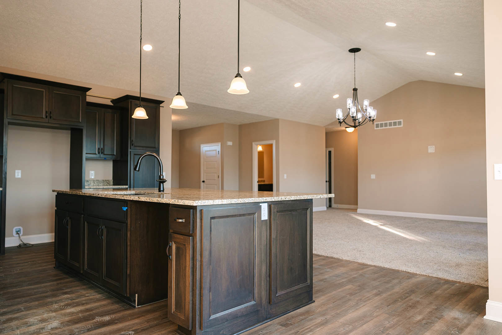 Spacious kitchen featuring a large marble-topped island, white cabinetry, stainless steel faucet, wood flooring, and recessed lighting