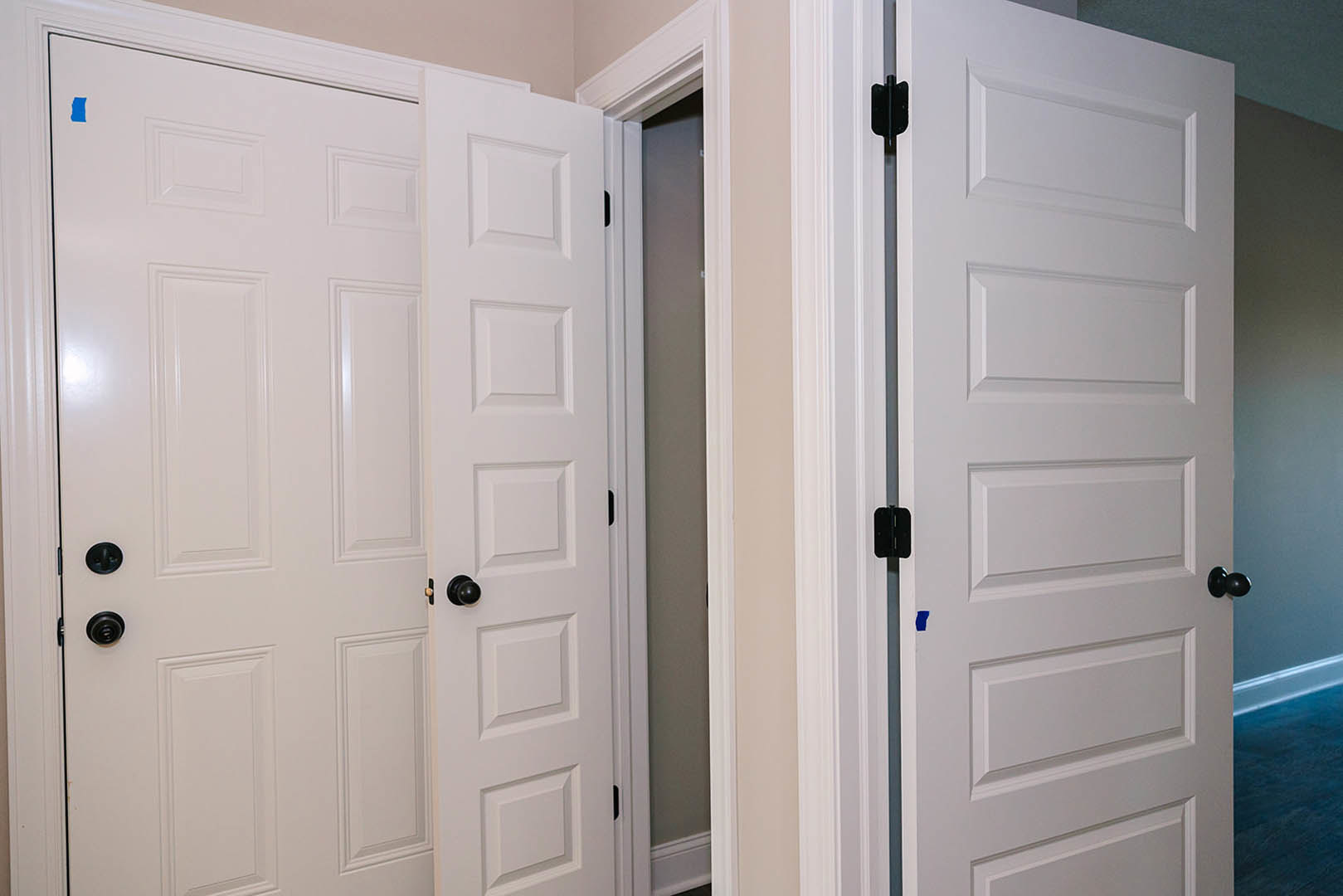 White paneled door with black knobs opening into a room with light-colored walls and trim