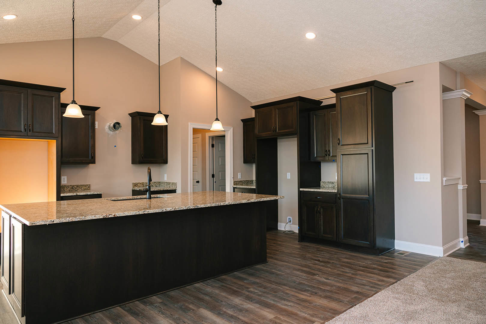 Spacious kitchen featuring a large central island with black base cabinetry, light countertops, modern pendant lighting, and sleek built-in cabinets against neutral walls