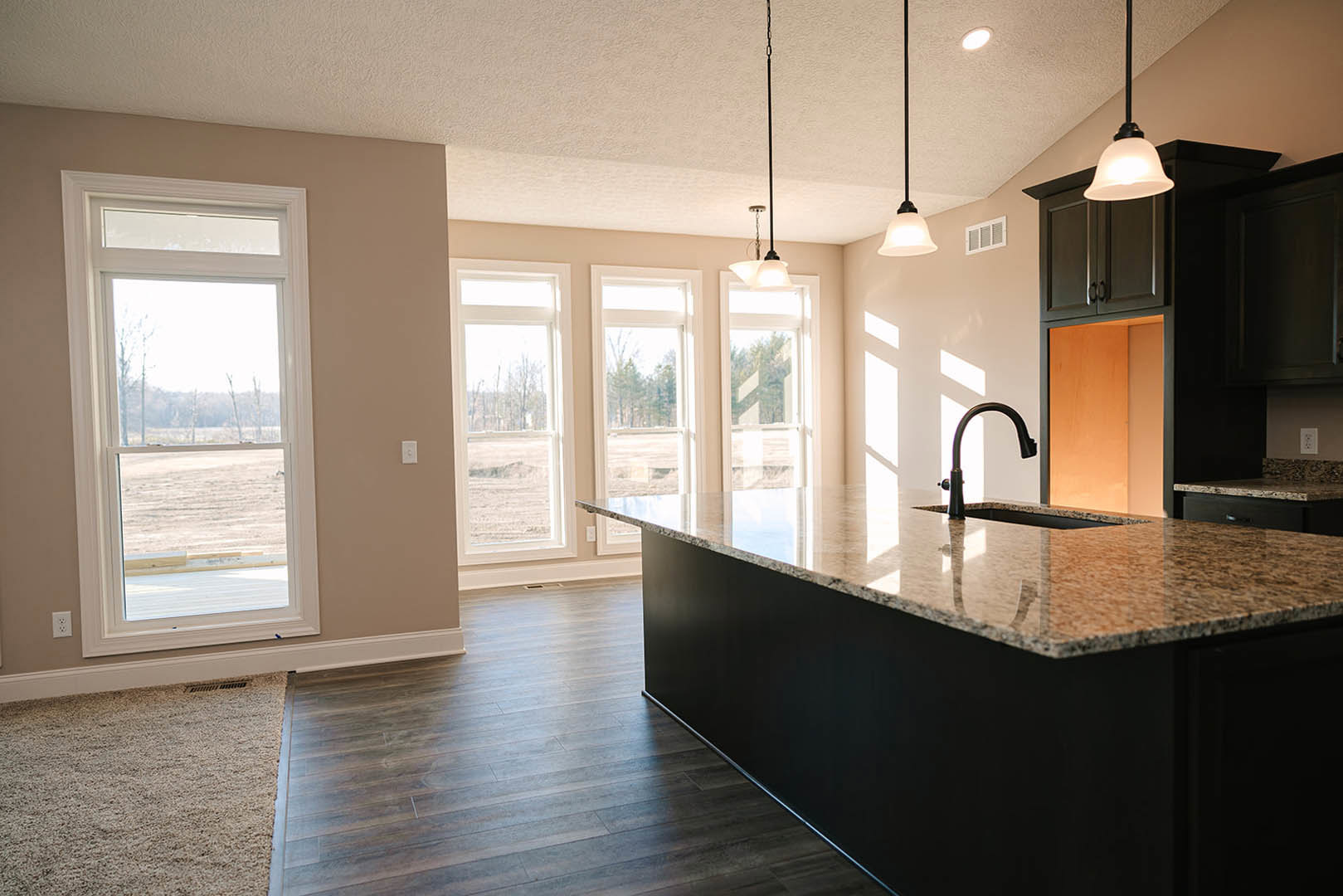 Kitchen with black island, black sink and faucet, black countertop, white ceiling, white wall vent, window overlooking outdoors, tile flooring, modern cabinetry