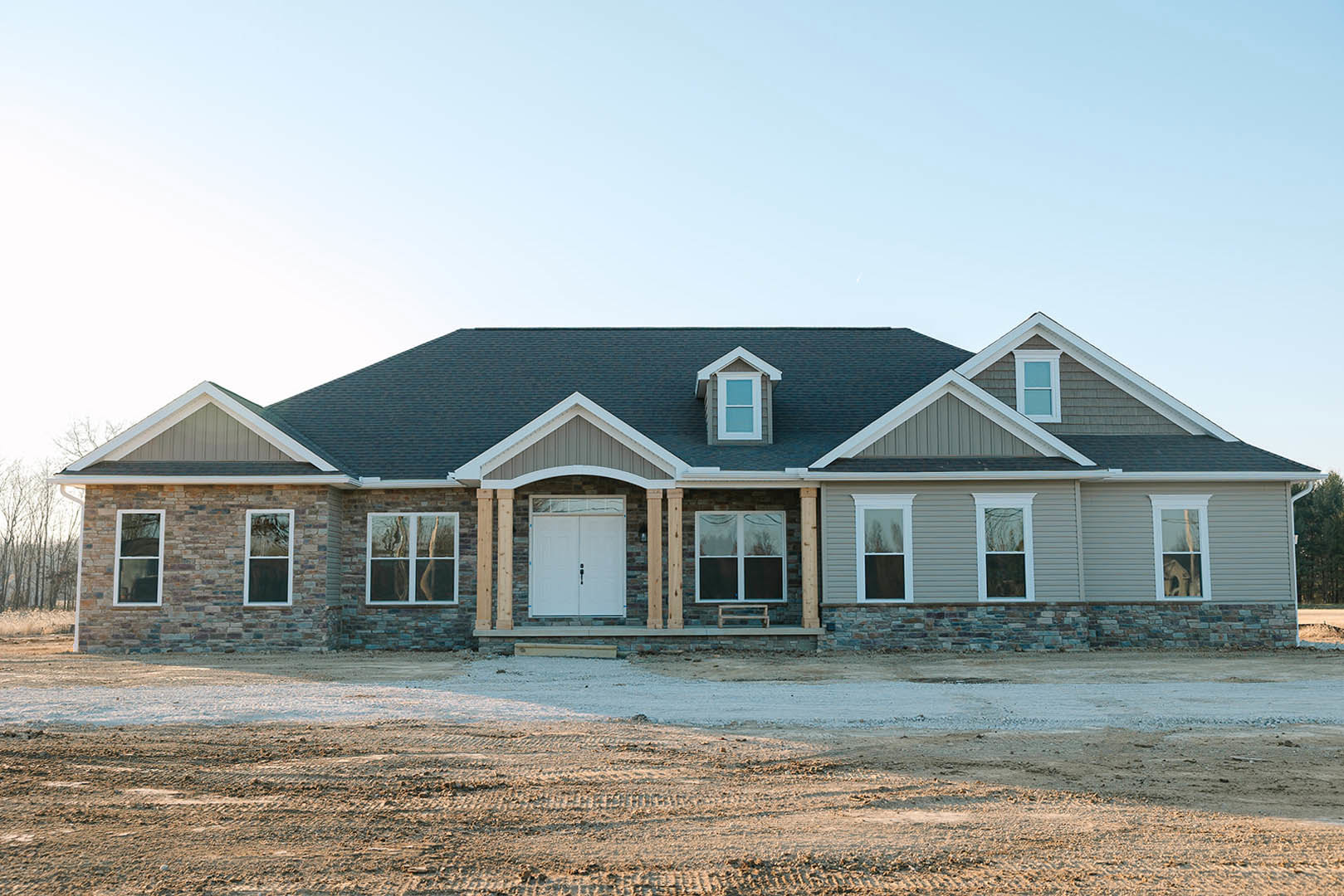 Partially built house with white double doors, window above, white-framed windows, and dirt road in foreground; tree reflected in window glass