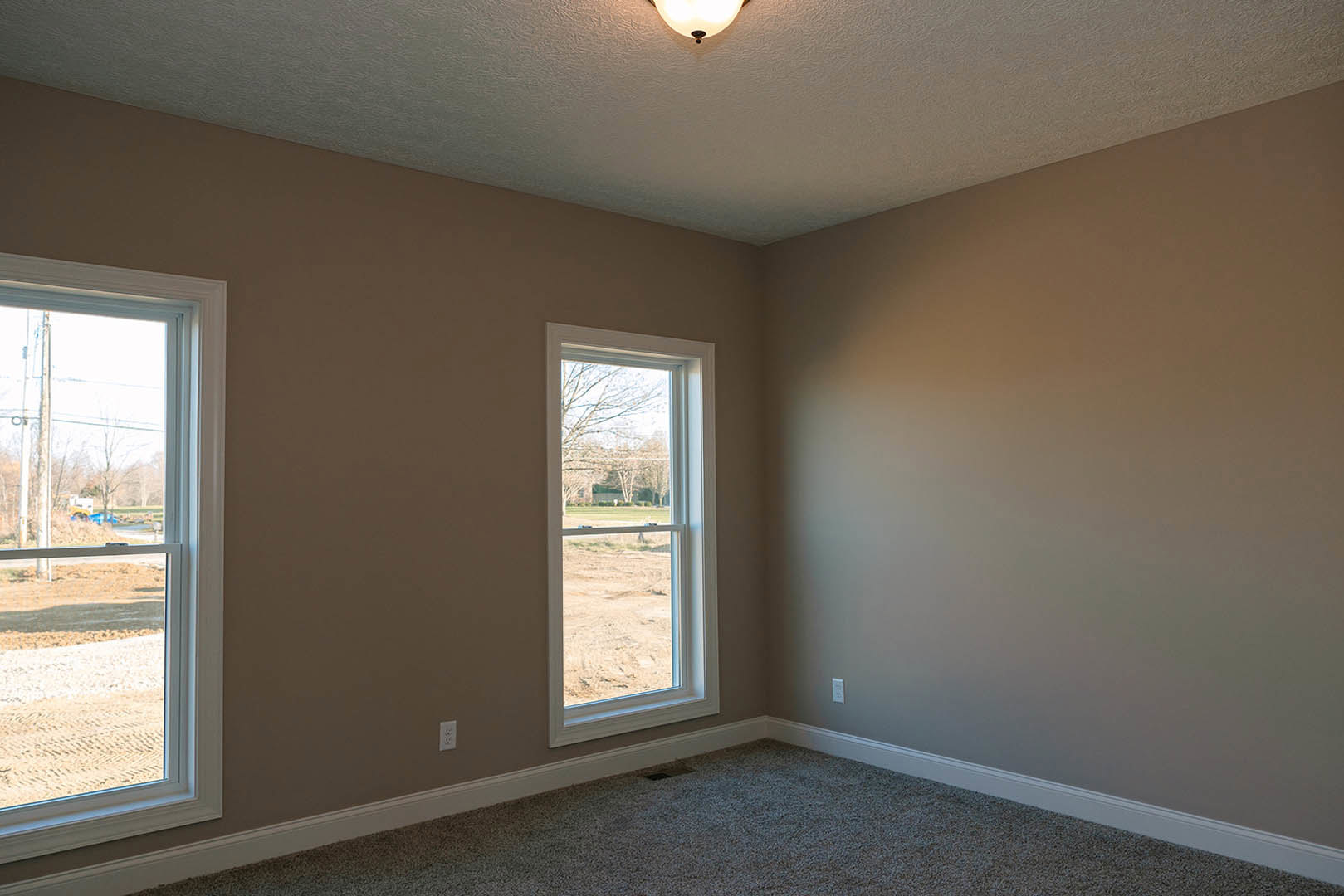 Bedroom with beige carpet flooring, white plaster walls, large window overlooking grassy field and trees, natural daylight, simple baseboard molding