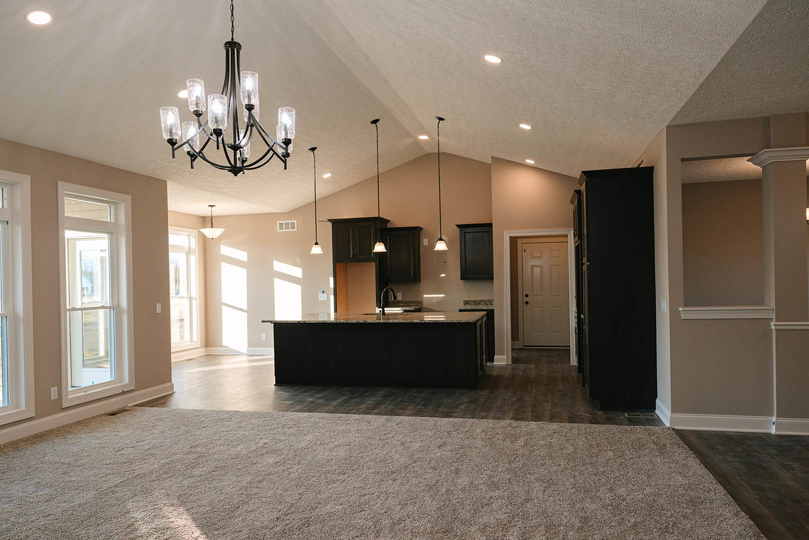 Open-concept kitchen and living room featuring a black countertop, white cabinetry, modern chandelier, white door with black hardware, large window, and light carpet flooring