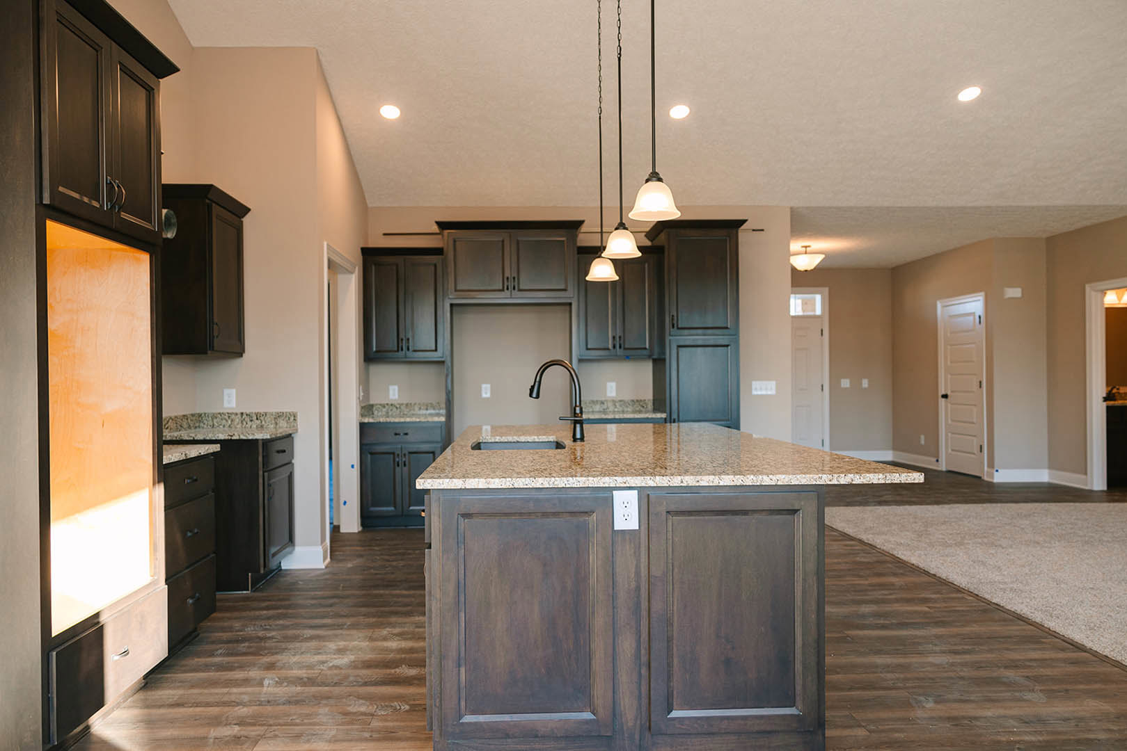 Spacious kitchen featuring a large granite island with built-in sink, white cabinetry, tile flooring, and a white door with black knobs