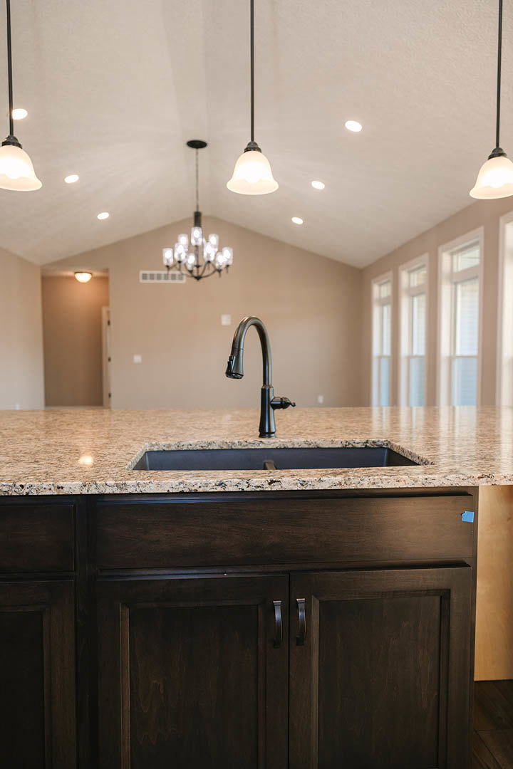 Granite countertop kitchen with black faucet, undermount sink, tile backsplash, white cabinetry, and chandelier hanging from ceiling