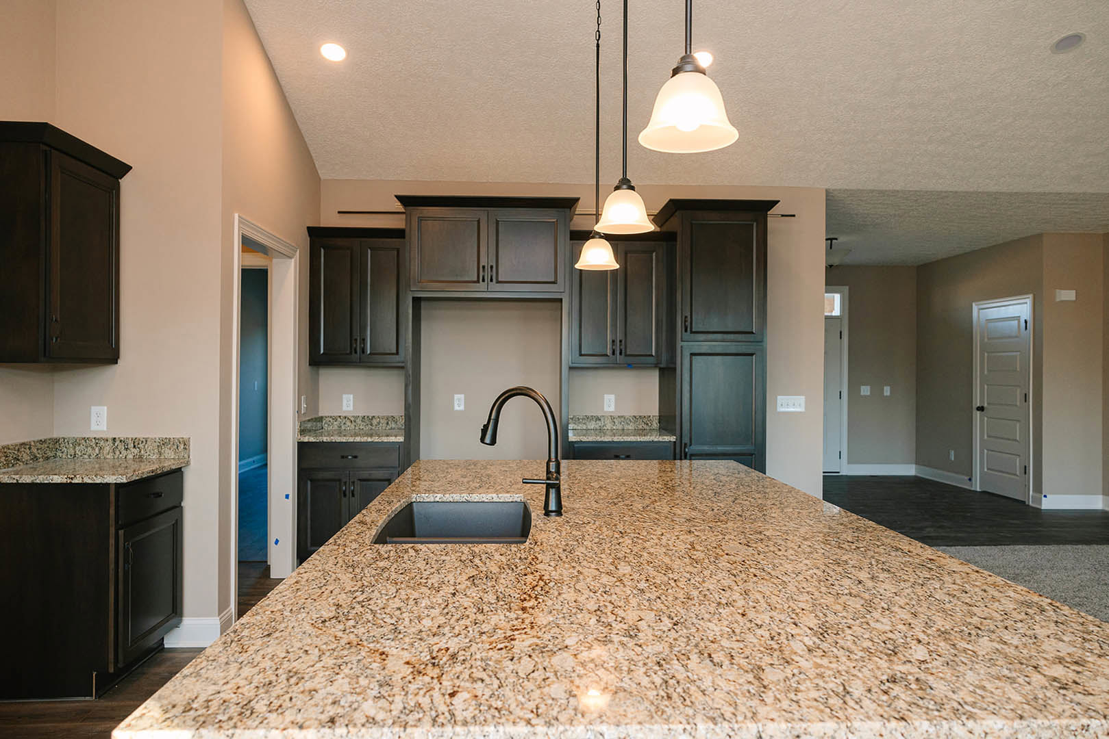 Modern kitchen with granite countertops, stainless steel sink and faucet, white cabinetry with black hardware, tiled backsplash, and a white door