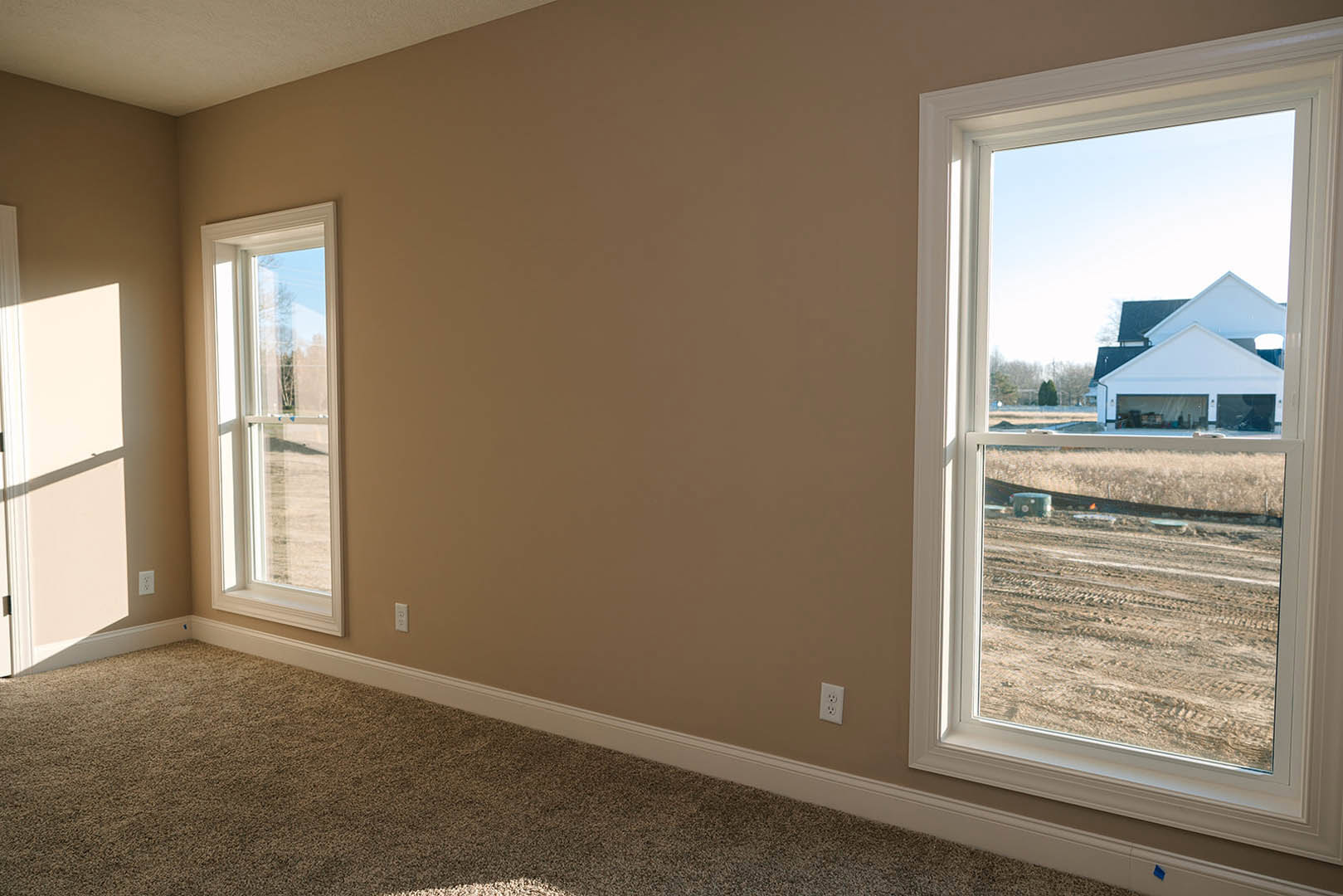 Carpeted room with two windows, white walls, and sunlight casting a door shadow across the floor