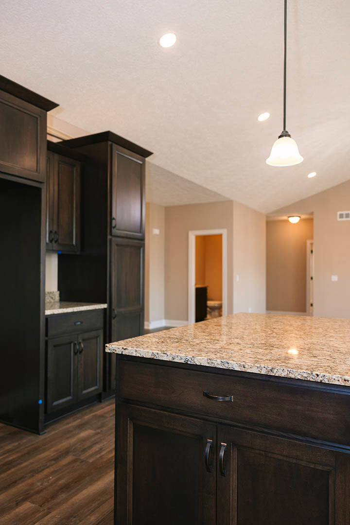 Marble kitchen island with waterfall edge, white cabinetry, stainless steel sink, and dark accent wall