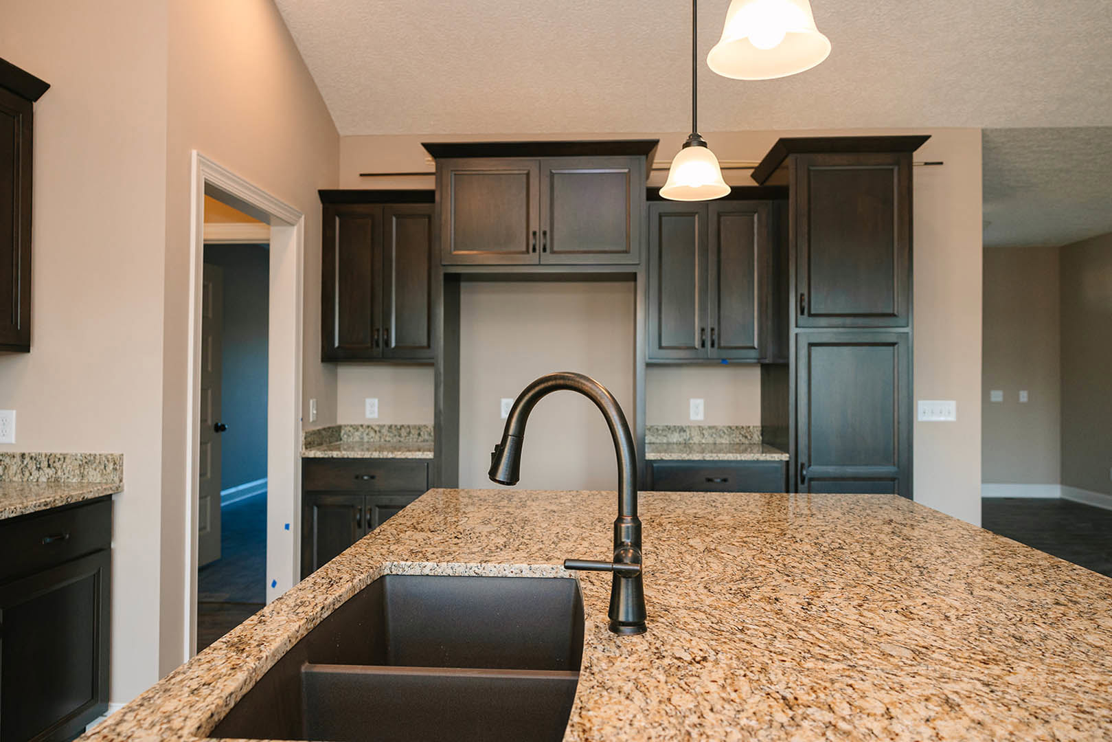 Modern kitchen with white tile backsplash, stainless steel sink and faucet, dark cabinetry with white trim, and stone countertop