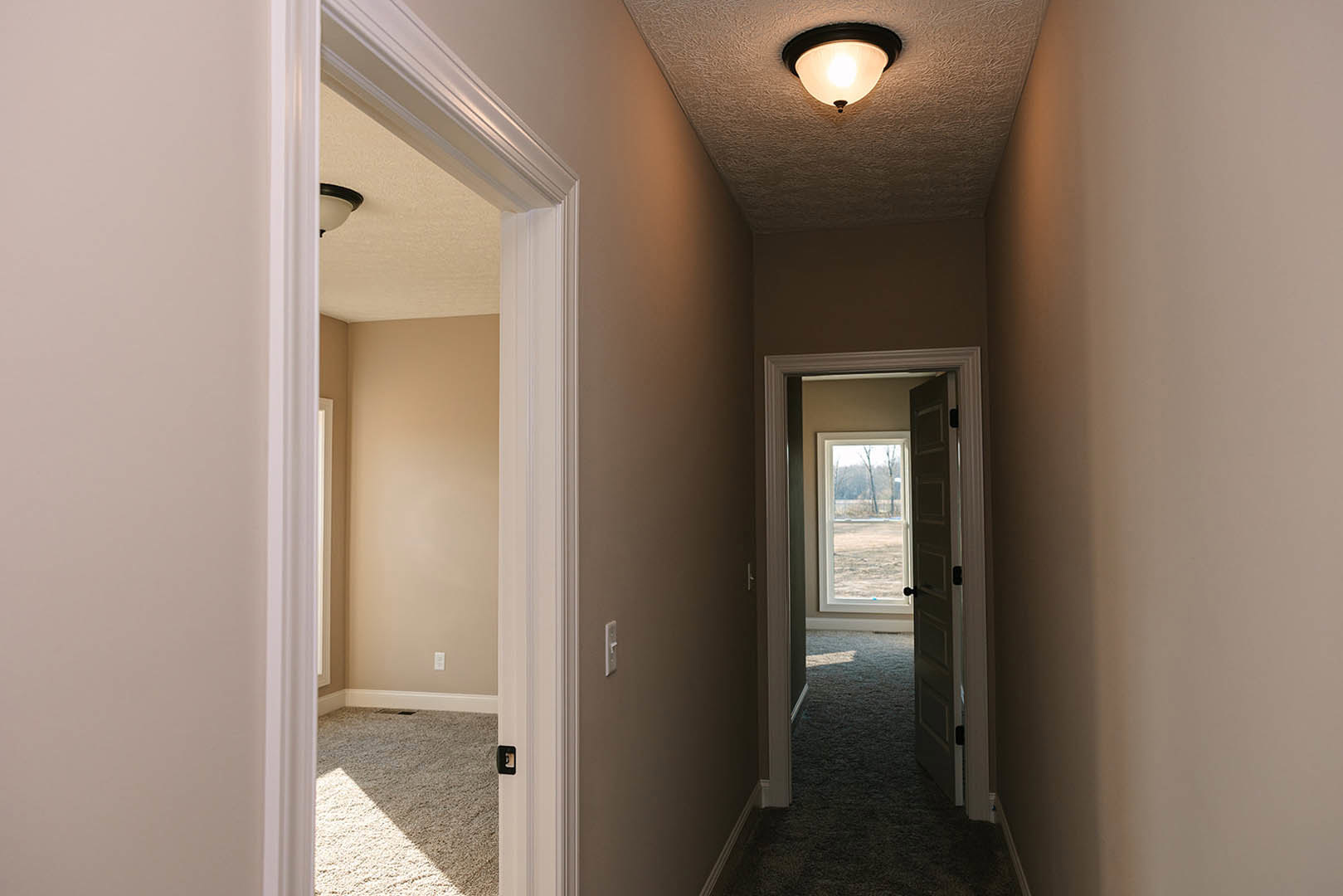 Hallway with white plaster walls, wood flooring, ceiling light fixture, open door revealing outdoor view, window letting in natural light