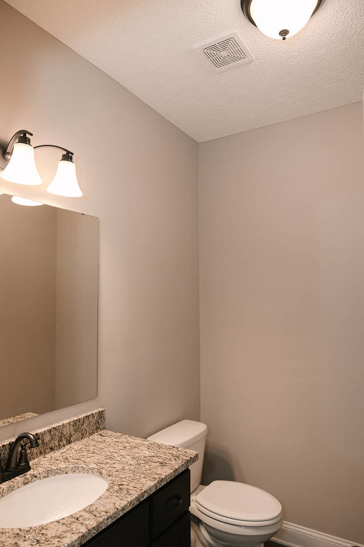 Marble countertop with undermount sink, large framed mirror above, white toilet beside vanity, recessed ceiling vent, chrome faucet, and modern light fixture in tiled bathroom.