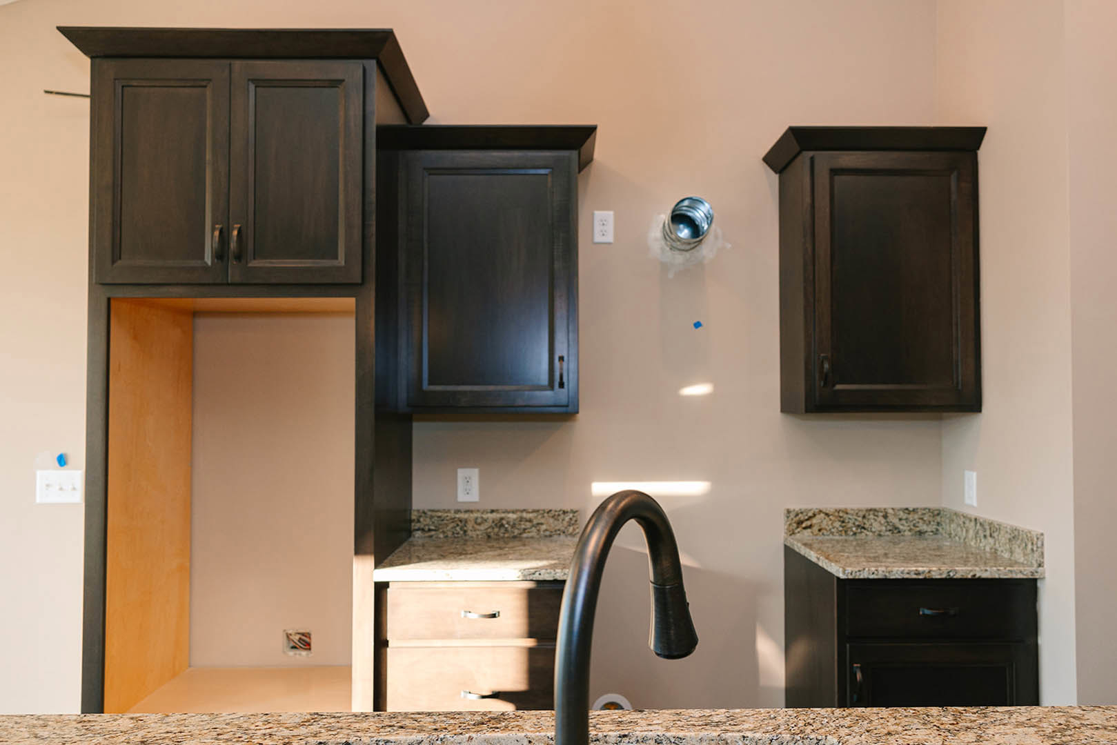 Dark wood kitchen cabinets with brushed metal hardware, stone countertop, stainless steel sink and faucet, open shelving, and built-in appliances.