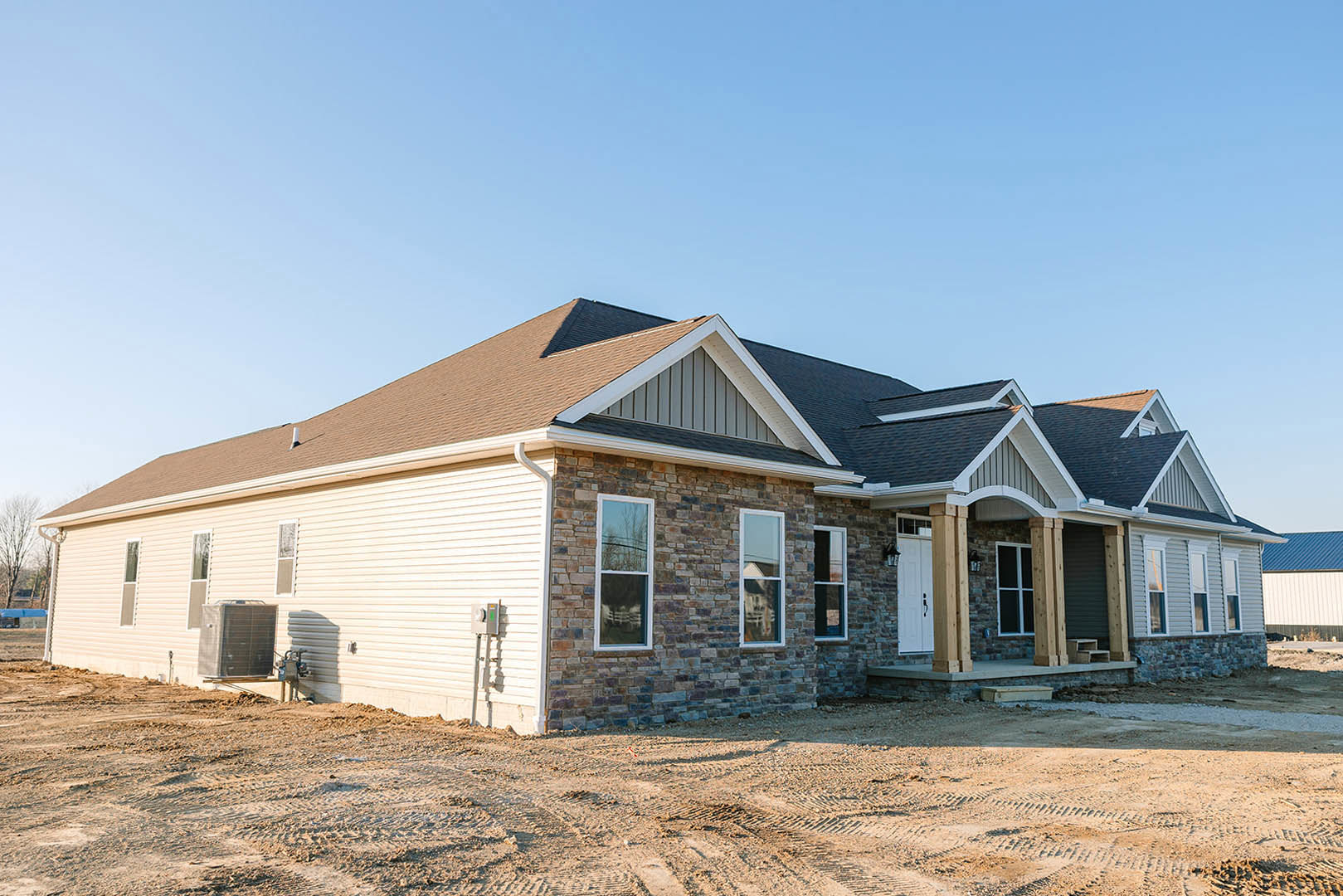 Partially built brick house with white-framed windows, exposed roof structure, and dirt construction site under clear blue sky
