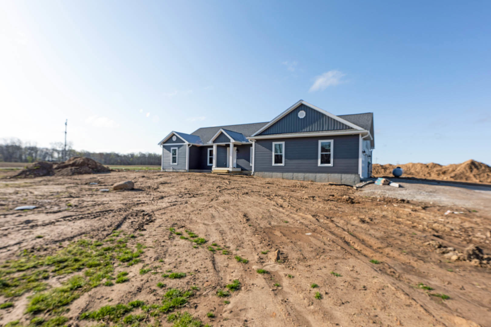 Partially built house with white door and window frames, surrounded by dirt field with sparse grass, under clear blue sky