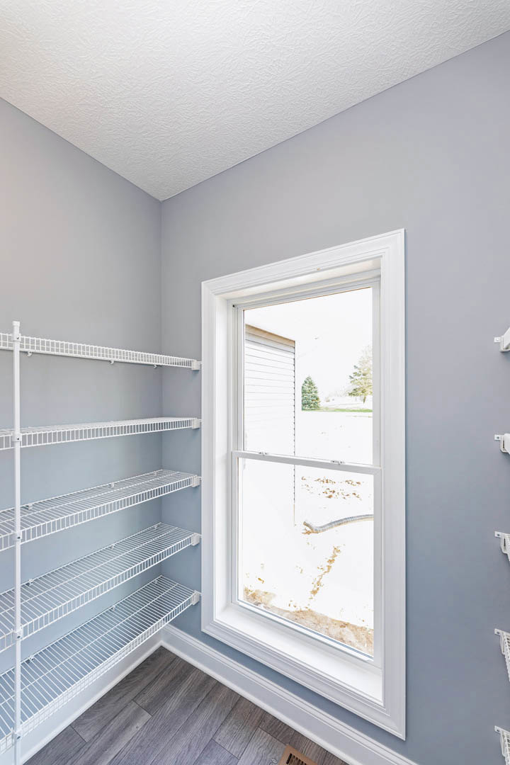 White wire shelving along a plaster wall, wood flooring, large window overlooking snowy yard
