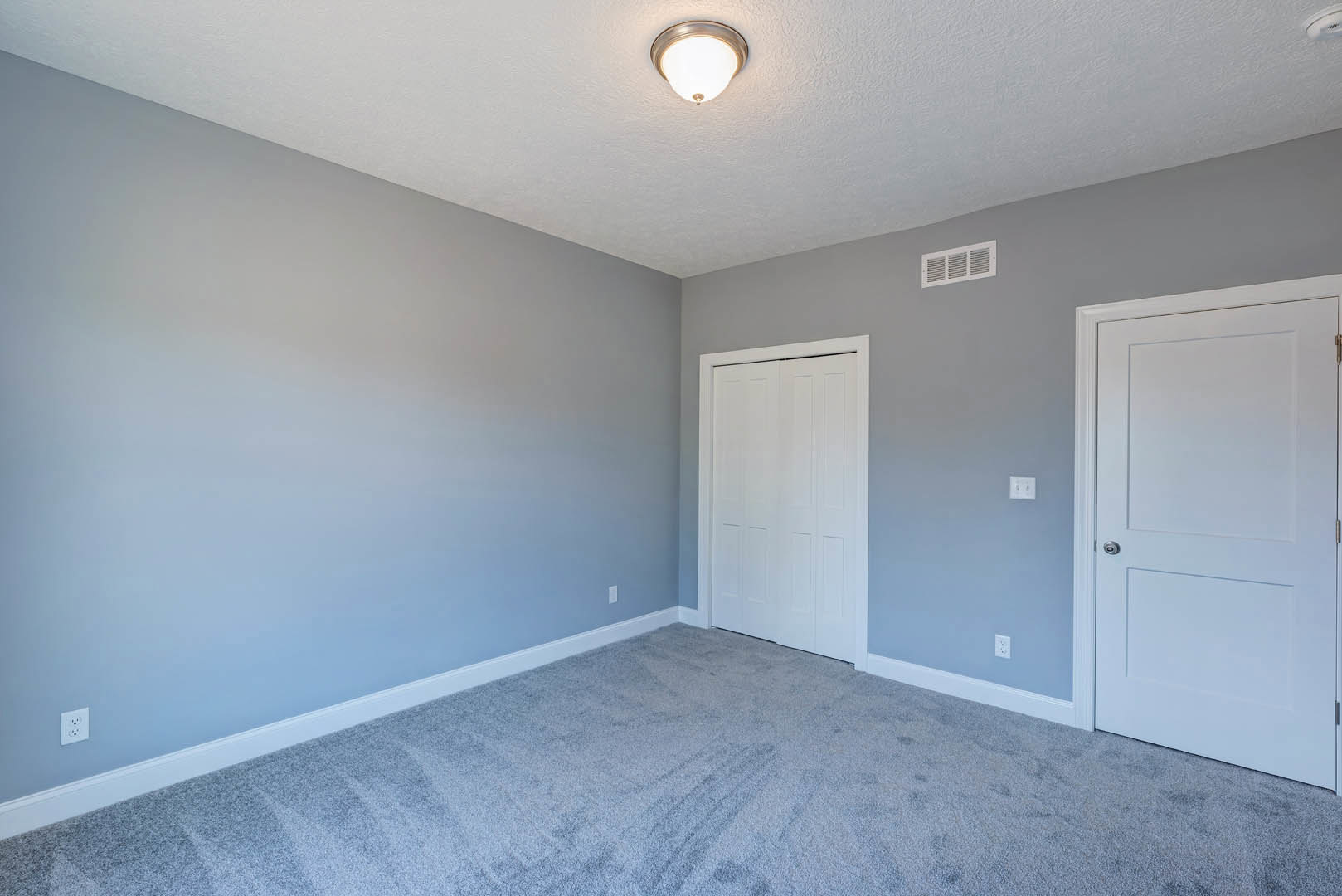 White paneled door with silver handle, beige carpet flooring, white walls, and flush ceiling light fixture in a residential room.