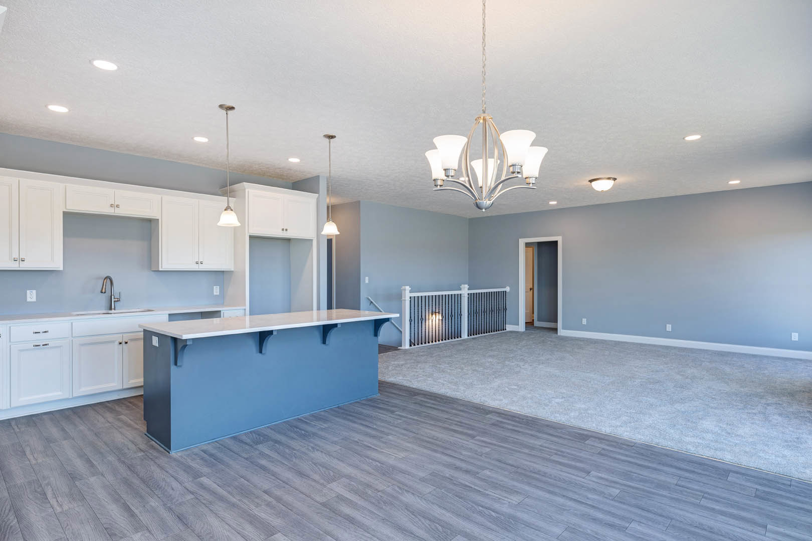 Open kitchen and bar area with blue accent wall, white railing, tile flooring, white cabinetry, sink, and two light fixtures including a five-light chandelier.