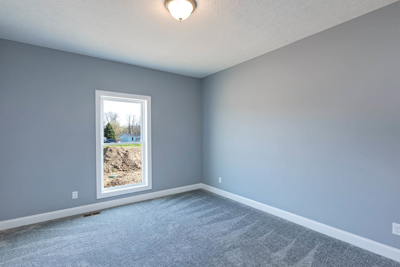Carpeted bedroom with white walls, large window overlooking yard, and recessed ceiling light